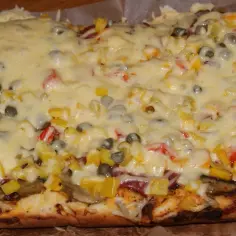 Pyszna pizza na grubym cieście z warzywami i roztopionym serem.