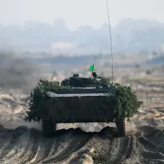 Czołg, zamaskowany gałęziami, pokonuje piaszczyste wzniesienie. Zielona flaga powiewa na jego wieży. Cały batalion przygotowuje się do manewrów.