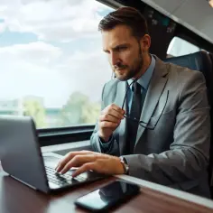 Biznesmen w garniturze pracuje na laptopie podczas podróży pociągiem. To jego delegacja do innego biura tej samej firmy.