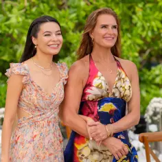 Brooke Shields i Miranda Cosgrove w kolorowych sukienkach na tle zieleni.