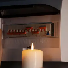 Kobieta sprawdza bezpieczniki przy świecy. W domu brak jednej fazy, co powoduje ciemność i niepewność.