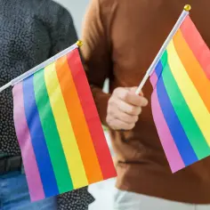 Dwie osoby trzymają tęczowe flagi, symbolizujące różnorodność i akceptację. Dyskusja o przyczynach biseksualizmu jest ważna.