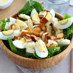 Sałatka Cezar z chrupiącymi grzankami, jajkiem i parmezanem, polana kremowym sosem do sałatki cezar.