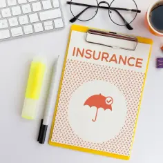 Ubezpieczenie zdrowotne bez pracy: dokument z napisem "INSURANCE" i symbolem parasola. Obok klawiatura, okulary, kawa.