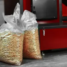Dwa worki z pelletem drzewnym na tle czerwonego kotła na pellet.