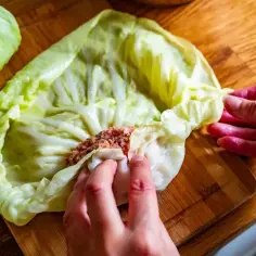 Ręce zwijają liść kapusty z farszem mięsnym, przygotowując gołąbki. To kluczowy etap w przepisie na gołąbki na 1kg mięsa.