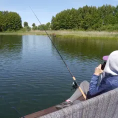 Osoba łowiąca ryby na spokojnym jeziorze, otoczona zielenią.