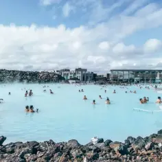 Ludzie kąpią się w turkusowej wodzie geotermalnej Blue Lagoon, otoczonej wulkanicznymi skałami i nowoczesnymi budynkami.