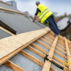 Pracownik montuje membranę pod blachę trapezową na dachu. Widać drewnianą konstrukcję i narzędzia.