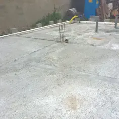 Plac budowy z nową wylewką betonową, gdzie widać, jak połączyć stary beton z nowym. W tle betonowa ściana i ogrodzenie.