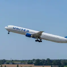 Samolot linii United Airlines wznosi się na tle błękitnego nieba nad krajobrazem.