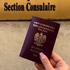 Dłoń trzyma polski paszport przed tabliczką "Section Consulaire". Czy do Amsterdamu potrzebny jest paszport?