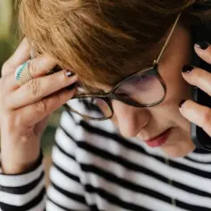 Kobieta w okularach rozmawia przez telefon, martwiąc się, czy pracodawca może rozporządzać urlopem pracownika.