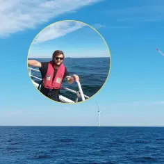 Mężczyzna w kamizelce ratunkowej na statku, na tle farmy wiatrowej na Bałtyku. To symbol **baltic power** i zielonej energii.