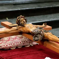 Drewniany Chrystus na krzyżu, przygotowany na wielki piątek w kościele. Leży na ozdobnej poduszce i aksamitnym obrusie.