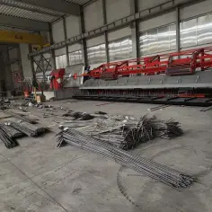Stalowe pręty zbrojeniowe leżą na hali produkcyjnej, gotowe do użycia. Maszyna do zbrojenia czeka na rozpoczęcie pracy, a cena robocizny jest kluczowa dla efektywności.