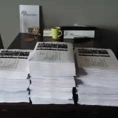 Stosy dokumentów na stole, obok nich dokument kancelarii adwokackiej. Gdy potrzebujesz pomocy, gdzie złożyć skargę na wspólnotę mieszkaniową, warto udać się do prawnika.