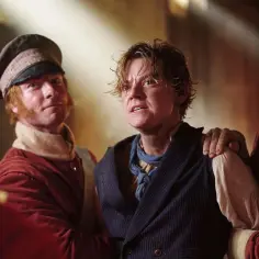 Młody mężczyzna, niczym **the artful dodger**, z wyrazem strachu na twarzy, jest trzymany przez dwóch mężczyzn w strojach z epoki.