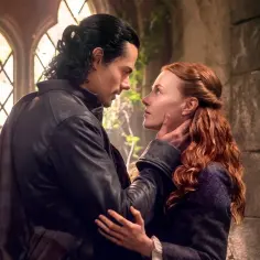 Mężczyzna z czarnymi włosami czule dotyka policzka kobiety o rudych włosach. Scena z serialu "Outlander: Krew z krwi".