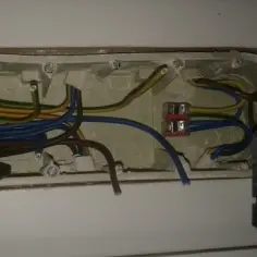 Widok wnętrza puszki instalacyjnej z podłączonymi przewodami elektrycznymi i częścią gniazdka.
