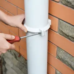 Montaż rury spustowej przy użyciu wkrętarki. Biały uchwyt mocuje rurę do ceglanej ściany.