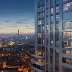 Nowoczesne osiedle apartamentowców w mieście nocą. Widać oświetlone okna, balkony z zielenią i panoramę miasta w tle.