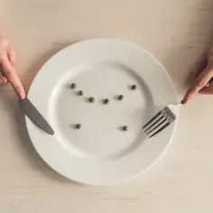 Dłoń z nożem i widelcem nad talerzem z kilkoma groszkami. Pica, czyli apetyt na nietypowe rzeczy, może objawiać się w dziwnych dietach.