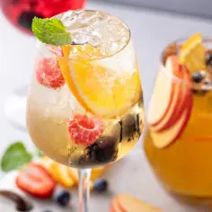 Orzeźwiający drink z prosecco i sprite, ozdobiony malinami, pomarańczą i miętą. Idealny na letnie popołudnie.