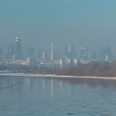 Widok na zamglone miasto z rzeką i lodem na pierwszym planie.
