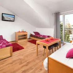 Pokój w domku wypoczynkowym Arka: dwa łóżka, stolik z krzesłami, TV i balkon.