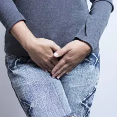 Osoba w dżinsach i szarej bluzce zakrywa dłonią pachwinę, sugerując problem z grzybicą pachwin.