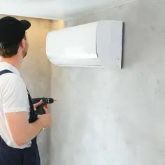 Instalator z wiertarką przy klimatyzatorze. Kluczowe jest, jak dobrać średnice rur do klimatyzacji, by zapewnić jej efektywność.