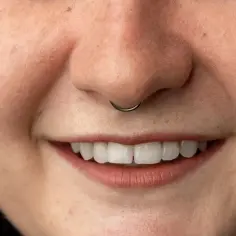Uśmiechnięta twarz z kolczykiem w nosie typu septum.