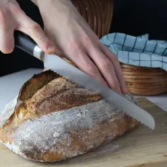 Ręce kroją świeży bochenek chleba na zakwasie na desce do krojenia.