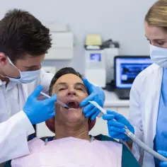 Dentysta podaje znieczulenie pacjentowi, asystentka używa ssaka.