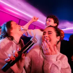 Grupa przyjaciół śmieje się i śpiewa karaoke przy neonowym świetle. Ich radość jest zaraźliwa, a każdy kolejny **bajm piosenki alfabetycznie** wywołuje jeszcze więcej śmiechu.
