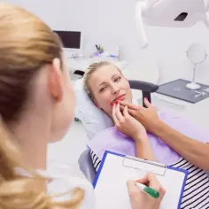 Kobieta w ciąży skarży się na ból zęba, wskazując go dłonią. Dentystka notuje objawy.