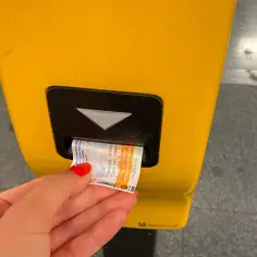 Ręka z czerwoną hybrydą wkłada bilet do żółtego automatu w praskim metrze. Bilety do metra w Pradze są łatwe do kupienia.