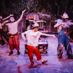 Barwna obsada teatru muzycznego w strojach cyrkowych, tańcząca w deszczu konfetti.