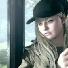 Młoda Rose Winters z Resident Evil w czapce z daszkiem patrzy przez okno autobusu, zamyślona.