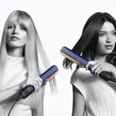 Dwie kobiety stylizujące włosy prostownicą Dyson Airstrait w kolorze granatowo-złotym.