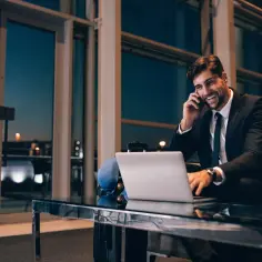 Biznesmen rozmawia przez telefon, pracując przy laptopie. Dowiedz się, kiedy przysługuje ryczałt za nocleg w delegacji krajowej i ile wynosi.