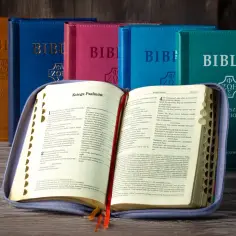Otwarta Biblia w fioletowym etui, na tle kilku Biblii w różnych kolorach.