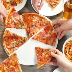 Ludzie sięgają po kawałki pizzy, frytki i piją piwo. Smaczna pizza, ale pamiętaj o jej kcal!