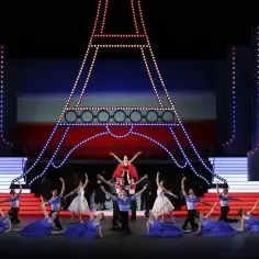 Tancerze baletowi na scenie z podświetloną Wieżą Eiffla. W tle czerwono-niebieska scenografia, przypominająca francuską flagę. To piękna aria, która porusza serca.