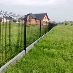 Nowy, czarny płot z podmurówką oddziela posesję z domem od zielonej łąki.