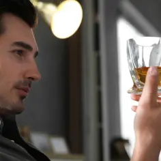 Mężczyzna zastanawia się, co zdrowsze: wódka czy whisky, trzymając w dłoni kieliszek bursztynowego trunku.