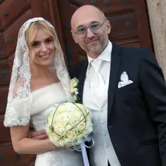 Szczęśliwa panna młoda z bukietem i jej mąż, w eleganckich strojach ślubnych, pozują przed drewnianymi drzwiami.