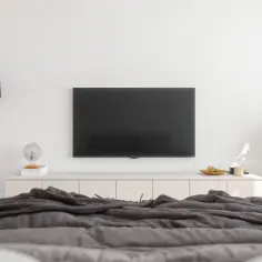 Nowoczesny salon z TV na ścianie, idealna wysokość od podłogi. Obok lampa, komoda z dekoracjami i roślina.