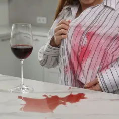 Plama z czerwonego wina na koszuli. Jak wywabić czerwone wino? Kieliszek wina i rozlana plama na blacie.